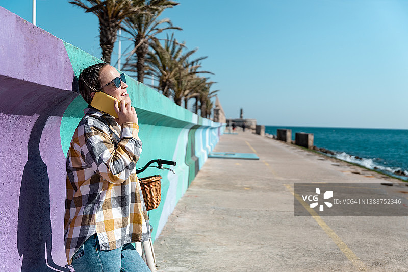 在彩色背景上微笑着用手机交谈的年轻女子图片素材