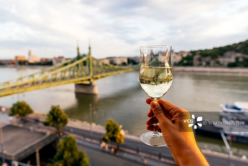 男人喝着气泡酒，欣赏着匈牙利布达佩斯多瑙河和自由桥的景色图片素材