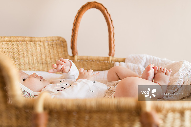 躺在海草摩西篮里，盖着舒适奶油色棉毯的14周大的男婴图片素材