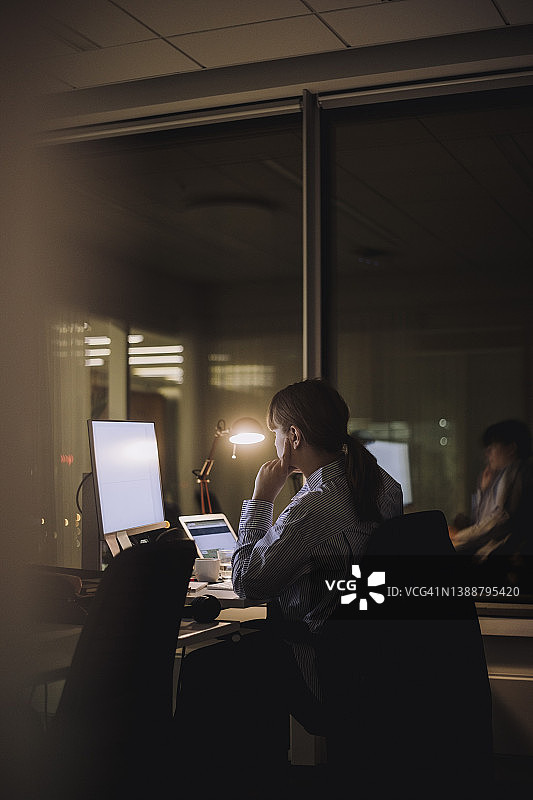 在办公室深夜用电脑工作的年轻女商人图片素材