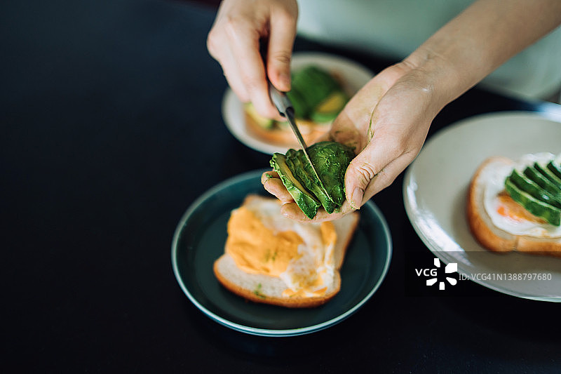 年轻亚洲女性在家中厨房切鳄梨片，准备健康的牛油果鸡蛋吐司早餐图片素材