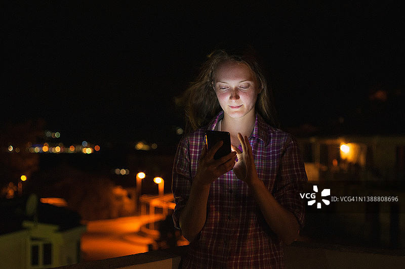 夜晚户外发短信的红发年轻女子图片素材