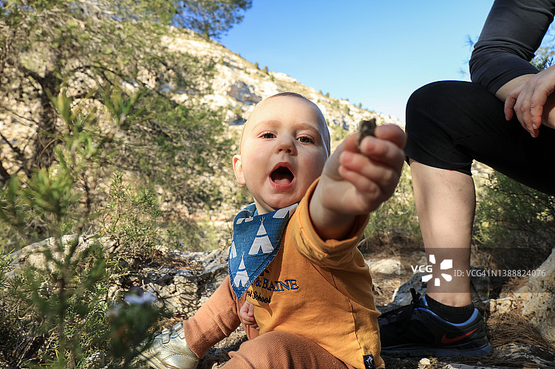孩子坐在森林里玩石头，并朝向相机方向递过去图片素材
