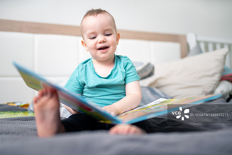 在父母床上看书的可爱小男孩图片素材