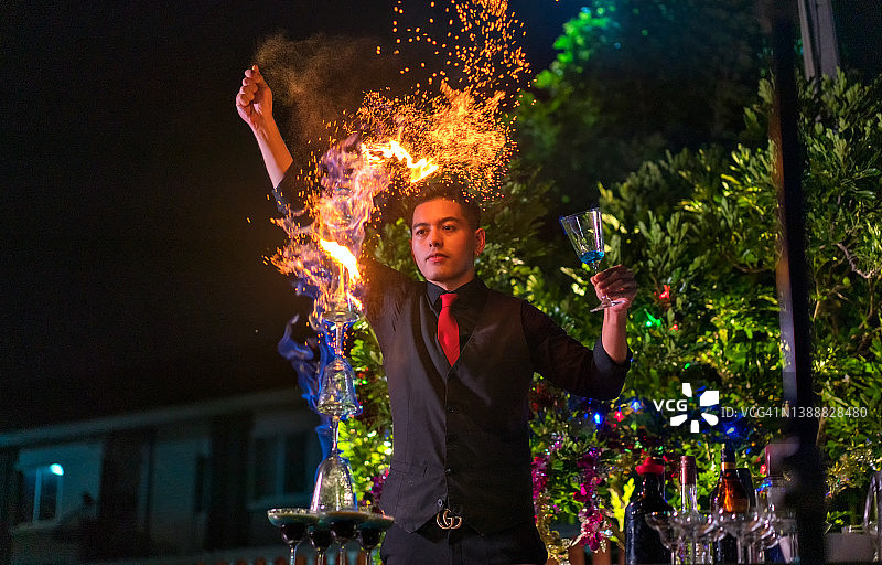 亚洲调酒师在火焰上撒肉桂粉，调制火焰兰博基尼鸡尾酒图片素材