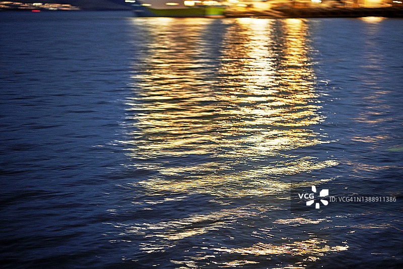 夜晚蓝色海浪上反射的橘色城市灯光图片素材