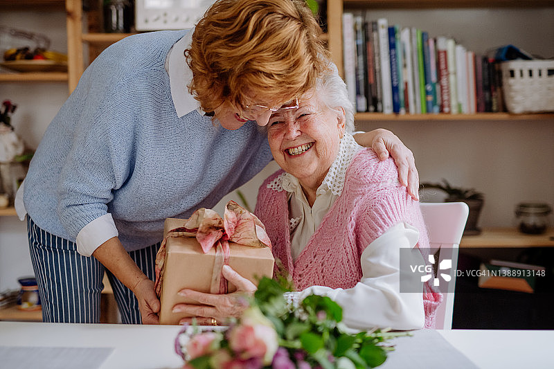 快乐的老年母亲在家收到成年女儿的礼物，母亲节概念图片素材