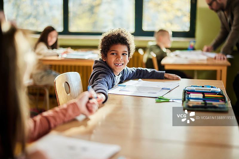快乐的黑人男学生在课堂上给他的朋友笔图片素材