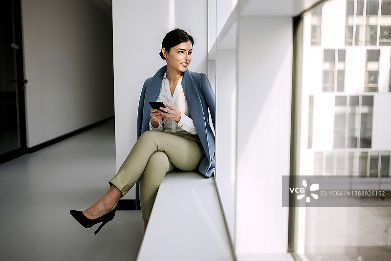 坐在办公室走廊窗边的年轻漂亮的商务女性图片素材