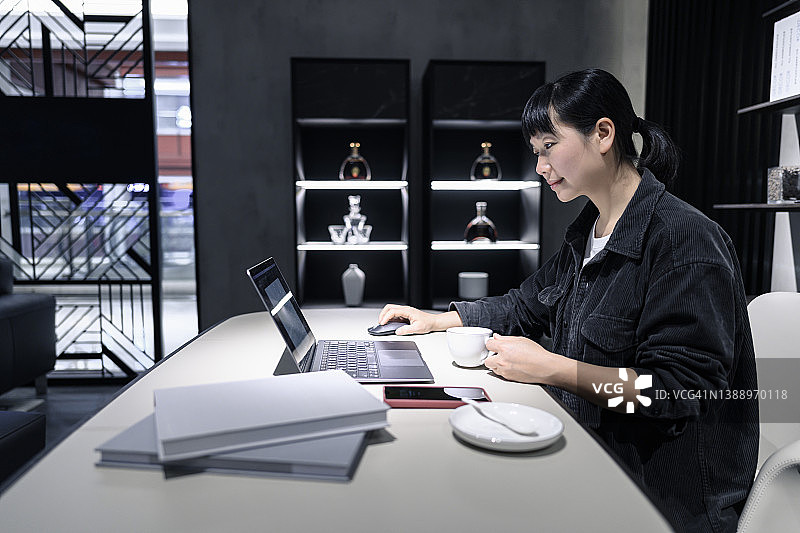 年轻女子在办公室喝咖啡，看着笔记本电脑图片素材