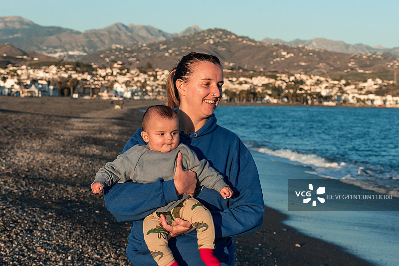 快乐的母亲带着宝宝在海滩上散步图片素材