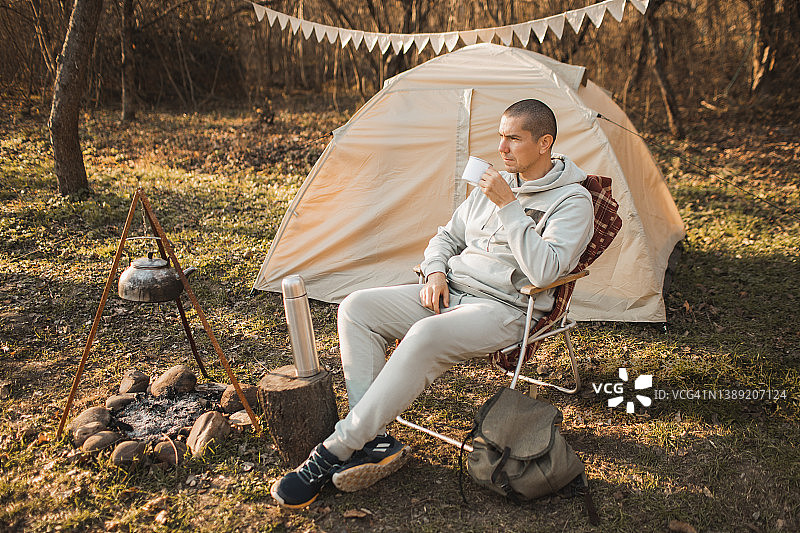 英俊男人在户外营地帐篷附近的折叠椅上喝茶图片素材