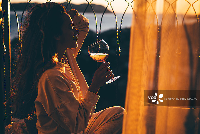 日落时在露台上喝葡萄酒的放松女人图片素材