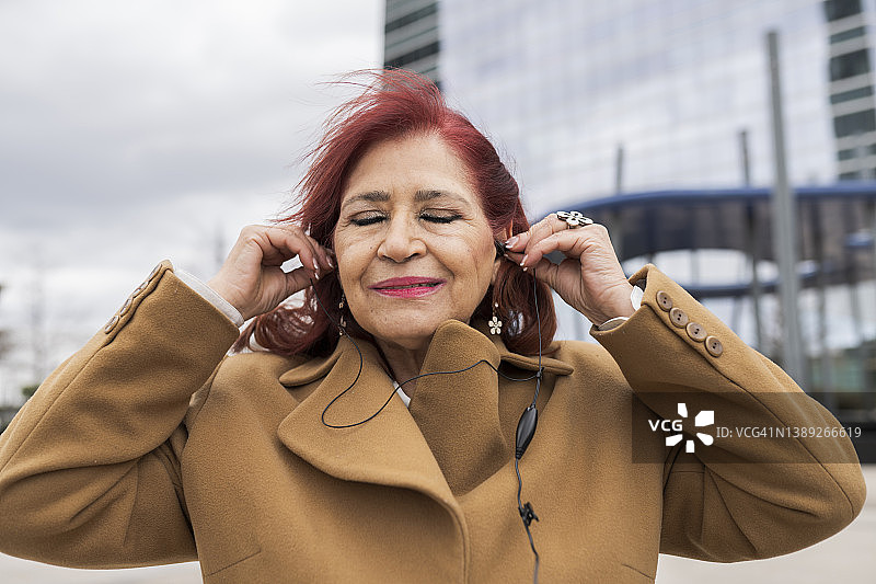 闭着眼睛在户外用耳机听音乐的漂亮中年妇女图片素材