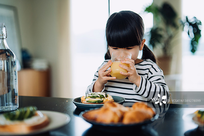 早餐时喝橙汁的亚洲小女孩图片素材