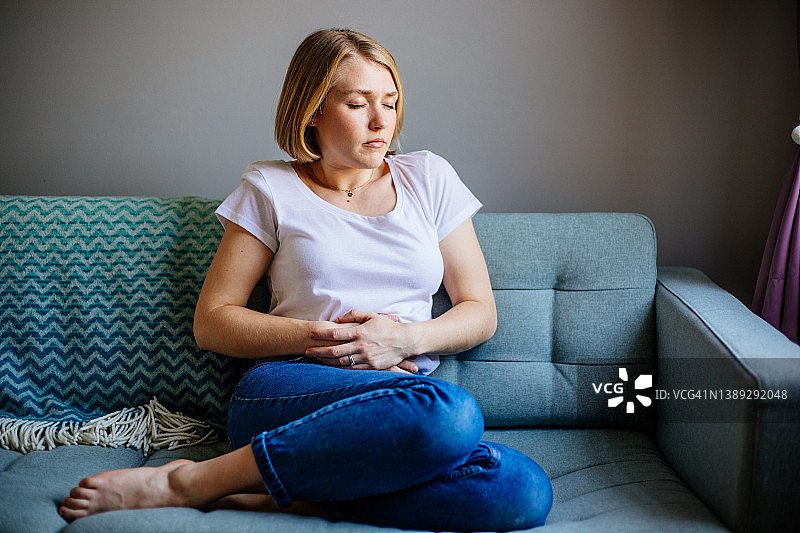 女人在家躺在沙发上时感到胃痛图片素材