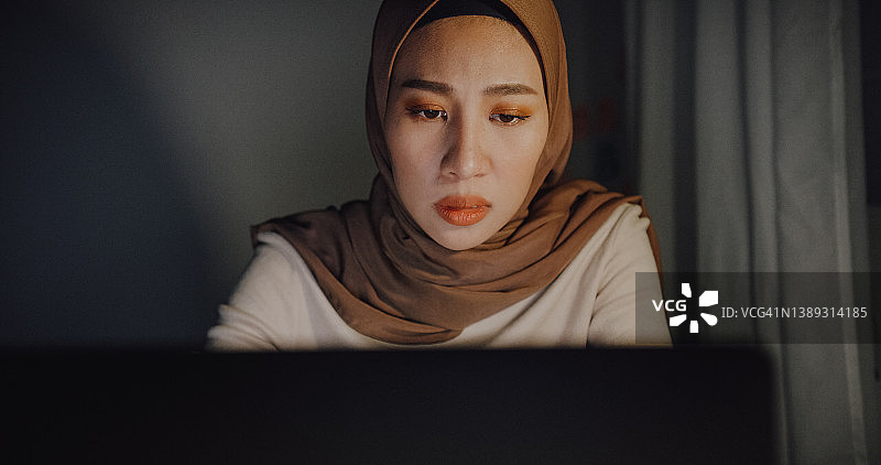 近距离拍摄戴着头巾的沮丧年轻亚洲穆斯林女商人，在家中办公室的桌子上使用笔记本电脑和平板电脑工作。图片素材