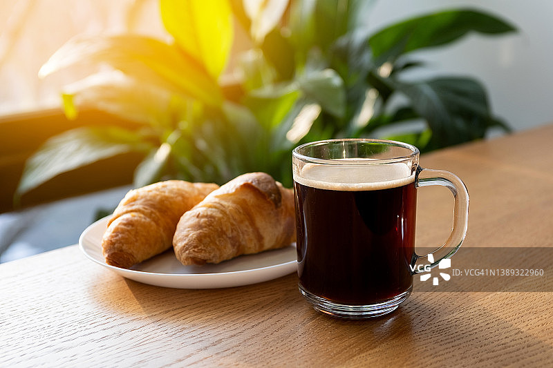 咖啡馆餐桌上的一杯黑咖啡，羊角面包，咖啡休息时间，早餐的概念，新鲜糕点图片素材