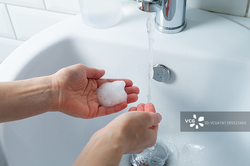 一名妇女在浴室、家中或公共场所用肥皂洗手消毒，预防疾病，讲究卫生。卫生概念，使用非接触式给皂机，遵守疫情和冠状病毒措施。图片素材