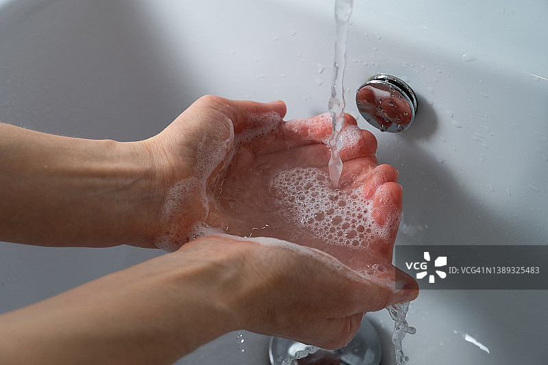 一名妇女在浴室、家中或公共场所用肥皂洗手消毒，预防疾病，讲究卫生。卫生概念，使用非接触式给皂机，遵守疫情和冠状病毒措施。图片素材