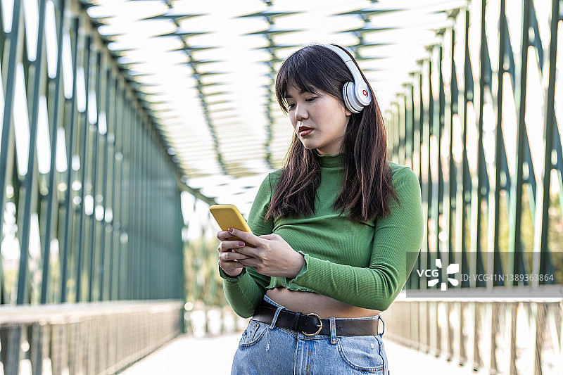 年轻女子戴无线耳机听有声读物的侧面照，背景为模糊的城市区域图片素材