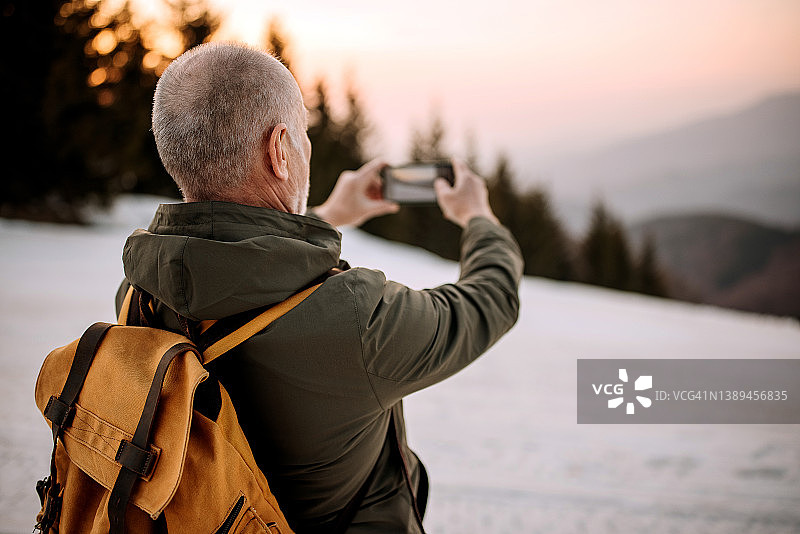 在山顶上用手机拍照的年长男人图片素材