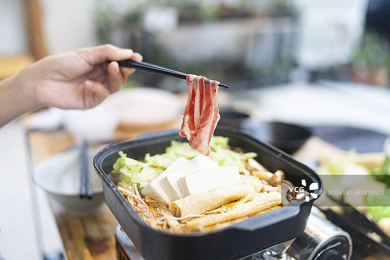 用筷子夹起肥牛片准备在迷你炉子上烹饪中式火锅的侧视图，提供送餐上门服务图片素材