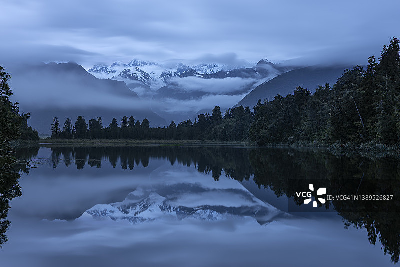 马瑟森湖，库克山和塔斯曼山脉在云中倒映在水中。湖泊周围环绕着温带雨林。新西兰西海岸地区，联合国教科文组织世界遗产地。图片素材