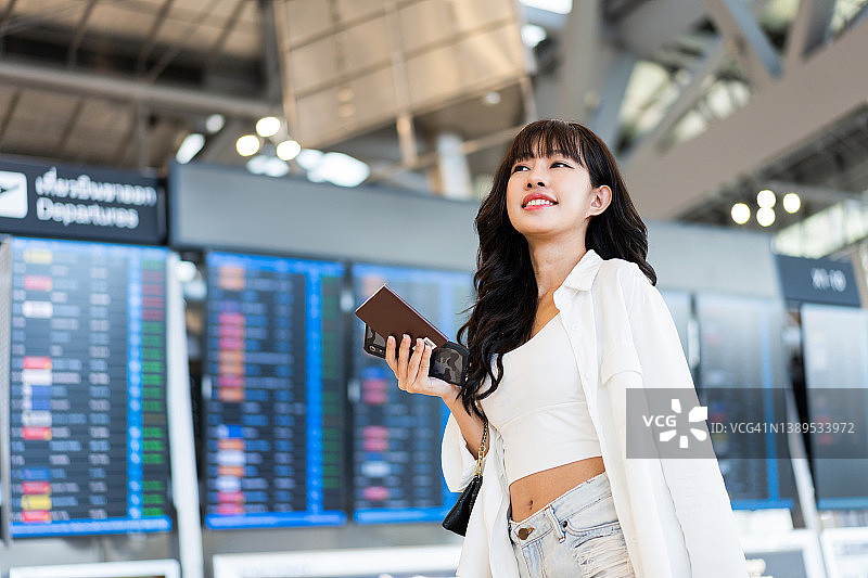 亚洲年轻女商人站在机场出发航站楼航班时刻表前的侧视图图片素材