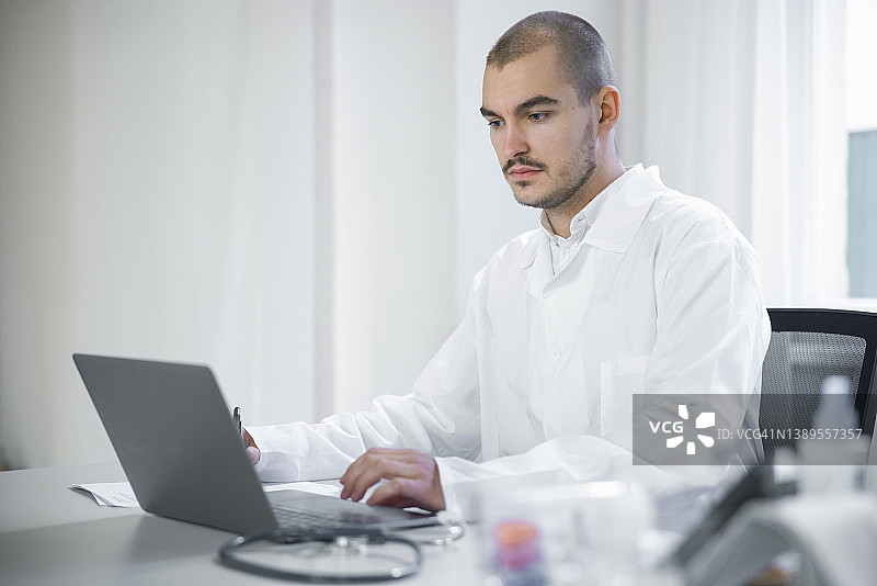 年轻男医生坐在办公桌前使用笔记本电脑图片素材