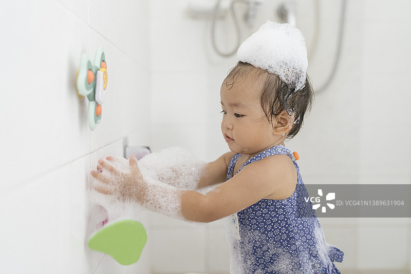 亚洲女宝宝在浴室浴缸里用洗发水洗头发的积极表情特写图片素材