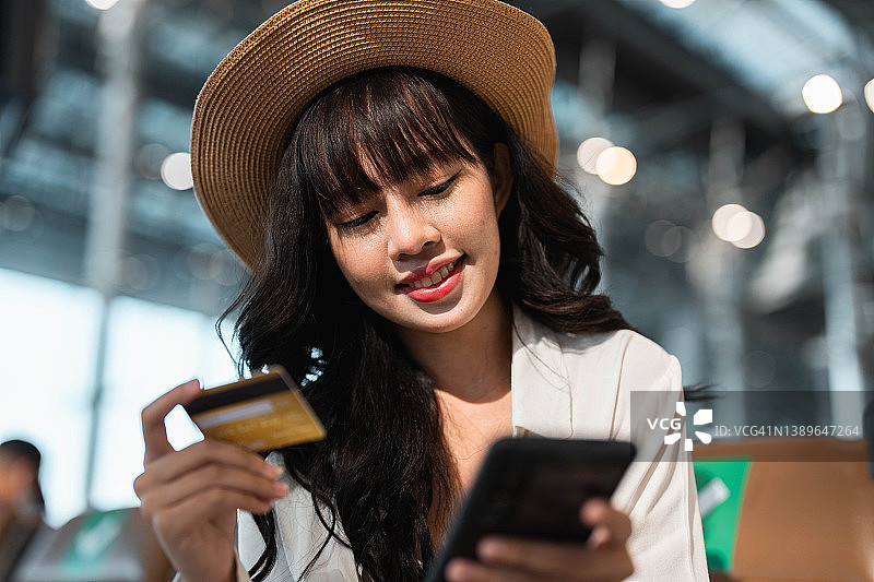 年轻亚洲女性在机场使用信用卡预订车辆/酒店图片素材
