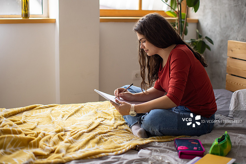 坐在床上在素描本上绘画的白人少女图片素材