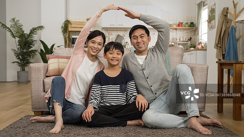 亚洲父母对着镜头微笑，和儿子在家中亲密地用手在头顶上做屋顶图片素材