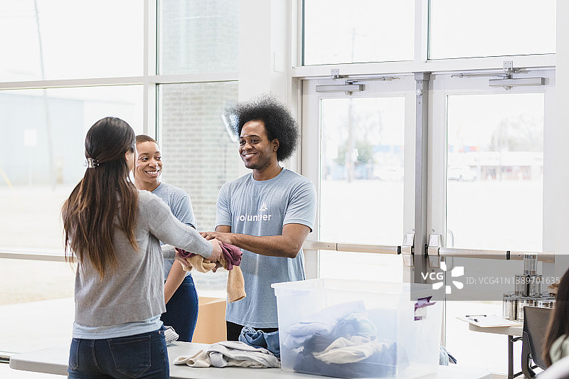 在衣物捐赠活动中做志愿者的夫妇向一位女士赠送免费衣服图片素材