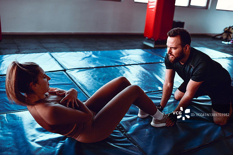 胡须健身教练帮助女运动员做仰卧起坐图片素材
