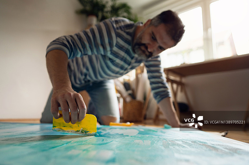 使用刮刀在画布上创作纹理的中年白人艺术家图片素材