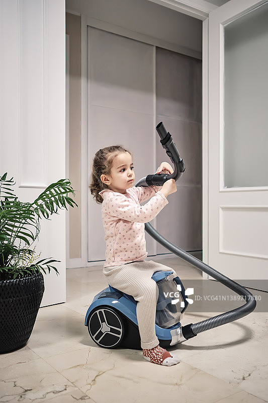 可爱女孩坐在家里的真空吸尘器上的 портрет图片素材