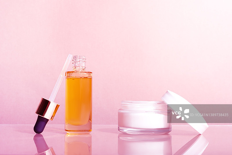 粉色背景上的玻璃滴管瓶和面霜罐图片素材