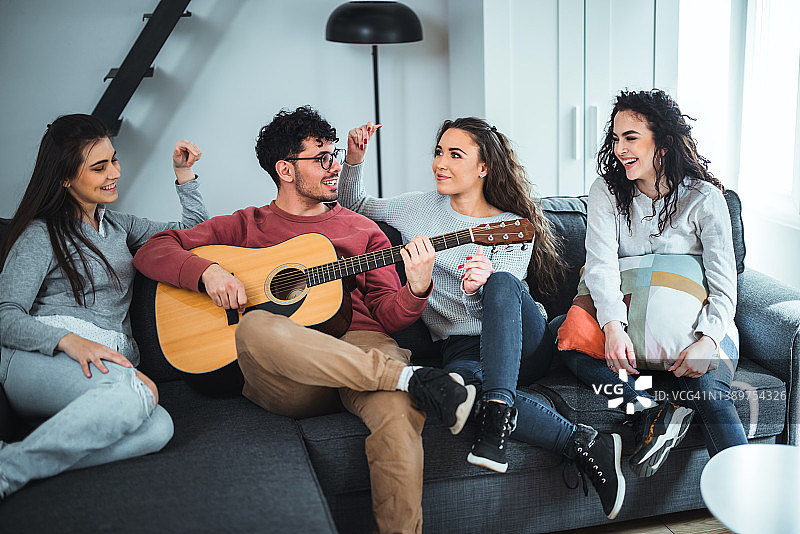 朋友们一起坐在沙发上休息，听其中一人弹吉他图片素材