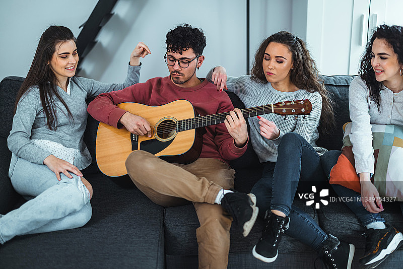 朋友们一起坐在沙发上休息，听其中一人弹吉他图片素材