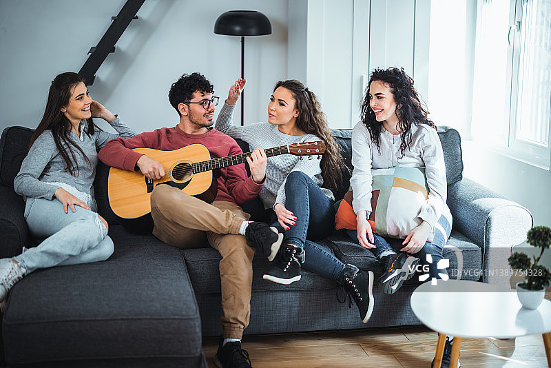 朋友们一起坐在沙发上休息，听其中一人弹吉他图片素材