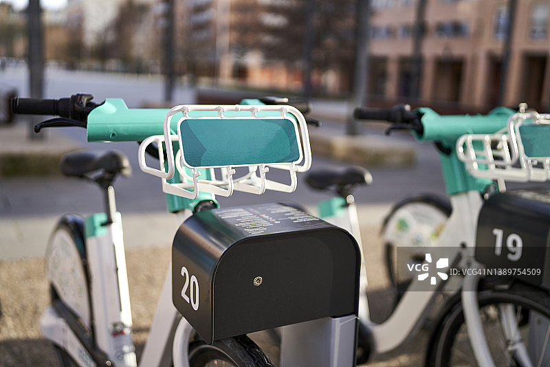 晴天城市充电租赁站的绿色和白色电动自行车，背景是砖砌建筑图片素材