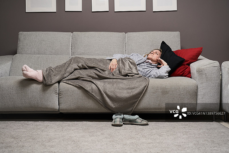白人女子睡在沙发上，盖着毯子的正面图。医疗保健概念。图片素材