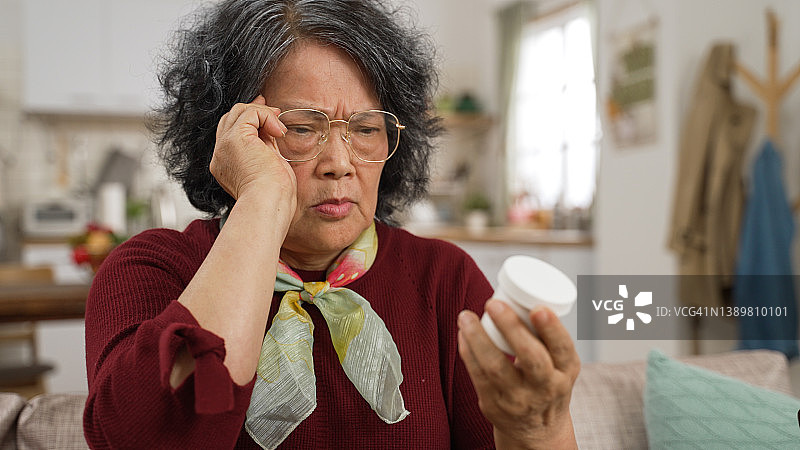 亚洲老奶奶老花眼困惑地拿着药瓶看说明书特写图片素材
