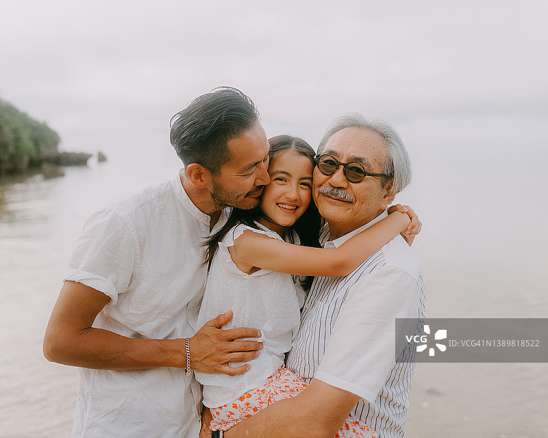 祖父、成年儿子和孙女在海滩上拥抱图片素材