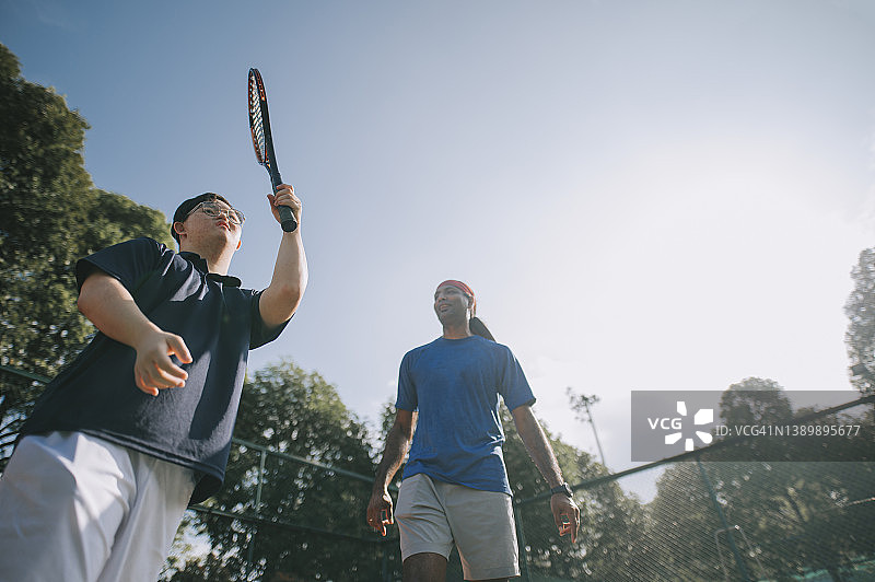 患有唐氏综合征的中国男子在周末早上学习网球图片素材