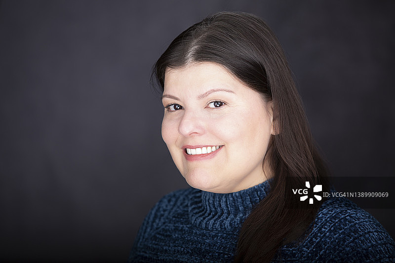 黑色背景上穿着蓝色上衣的美丽拉丁女士的头像。她站在她的右边。她微笑着。图片素材