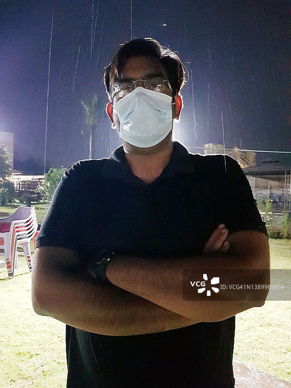 男子戴着口罩站在雨中，手臂交叉看着镜头的肖像照图片素材