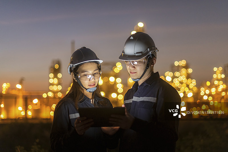夜班工程师在炼油厂讨论平板电脑计划，注意安全设备和团队合作图片素材